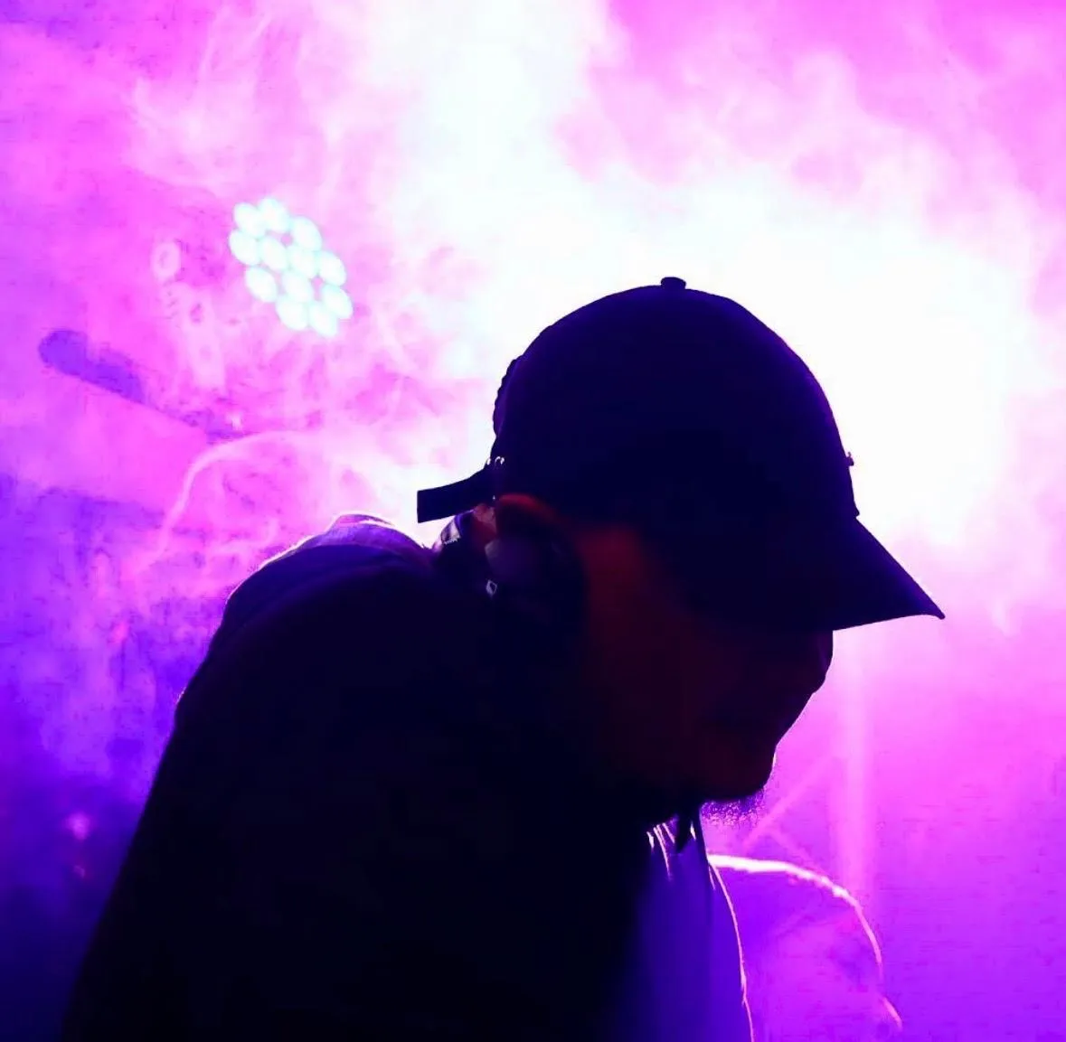 A DJ in silhouette against pink smoke and a stage light