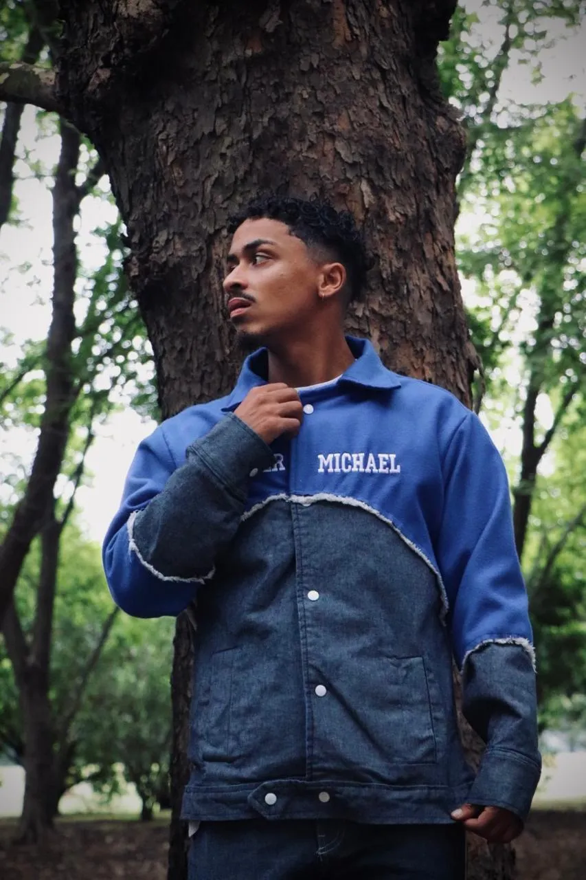 A man in a two-tone Carter Michael denim jacket looking away, against a tree trunk