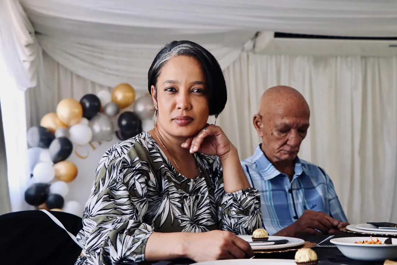 A woman resting her chin on her hand at a dinner table, with balloons behind her