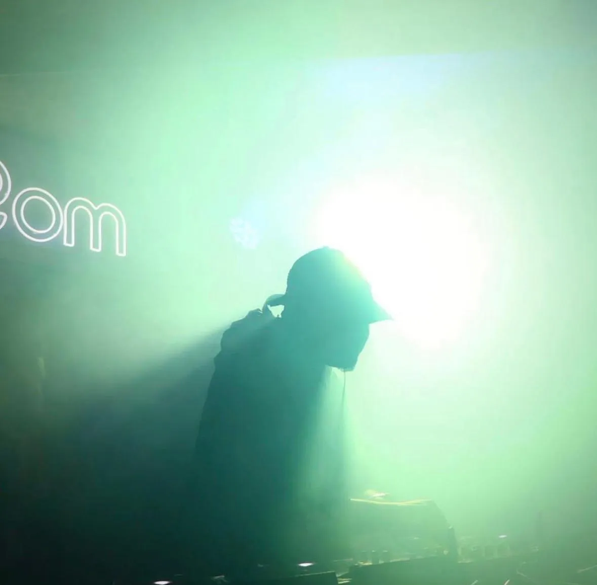 A DJ in silhouette against bright green haze